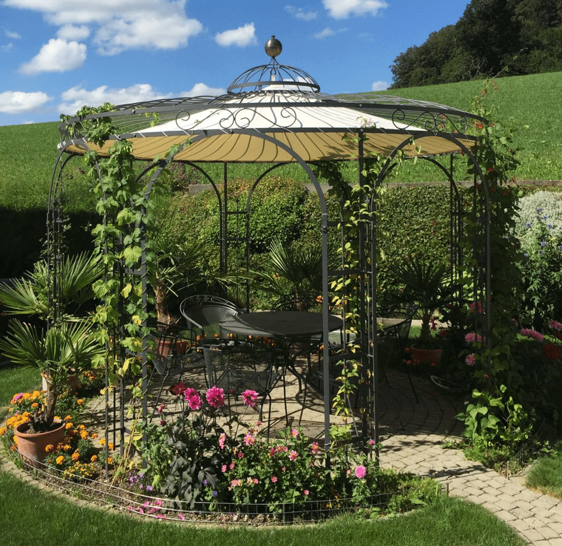 Gartenpavillon Florenz mit Messingkugel und Sonnensegel in pulverbeschichtet anthrazit umgeben von bluehenden Pflanzen