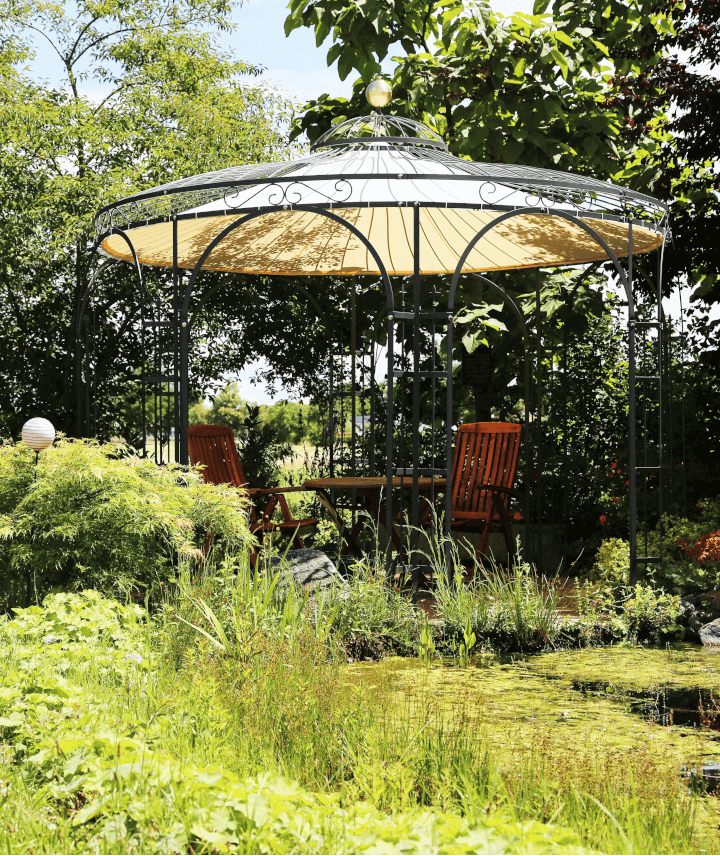 Pavillon Florenz in pulverbeschichtet anthrazit mit Messingkugel und Sonnensegel hinter einem Gartenteich